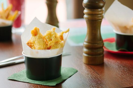 Pakora rolled to parchment in a black cup, over a wooden table, great image for your needs.