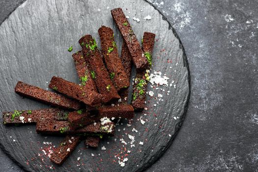 Black bread toast for beer with garlic salt and herbs on a black background