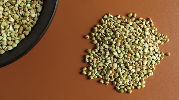 Raw green buckwheat in a brown clay plate on a brown background. Vegan organic food concept. The concept of diet, weight loss, healthy and proper nutrition. Copy space for text. Top view, flat lay.