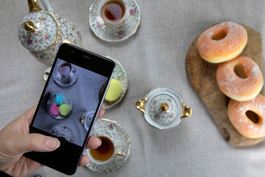 Top view picture of lady,blogger sitting in cafe and making photo with mobile of food, afternoon tea with doughnuts and macarons on the table high angle, food and social media concept close up