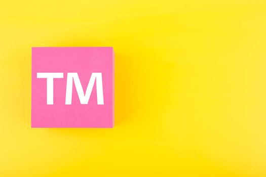 TM trademark sign on pink figure on yellow background with copy space. Concept of intellectual property registration and protection