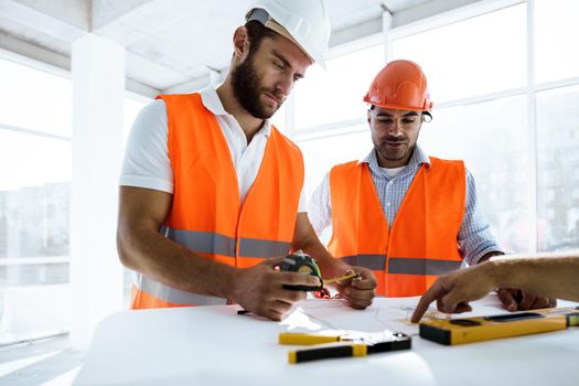 Two young engineers man looking at project plan on the table in construction site