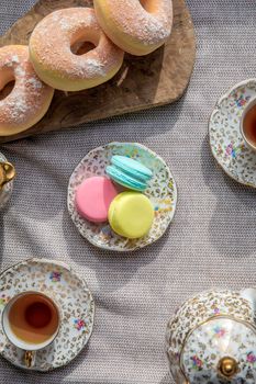 Cup of tea and macarons on diner table, antique tea pot set and doughnuts for afternoon tea top view colorful