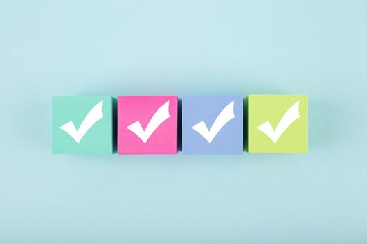 Four checkmarks on multicolored cubes in a row on blue background with copy space. Concept of questionary, checklist, to do list, planning, business or verification. Modern minimal composition