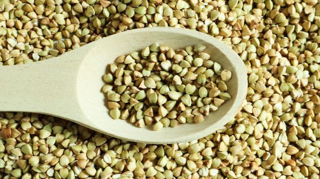 Buckwheat scattered background, raw green cereal in a wooden spoon. Healthy groats. Organic raw non-fried vegetarian food. The concept of a healthy and balanced diet. Diet product. healthy groats
