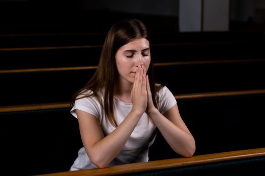 A Christian girl in white shirt is sitting and praying with humble heart in the church.