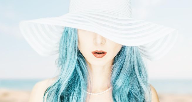 Portrait of stylish beautiful woman in a hat with wide brim on background of beach.