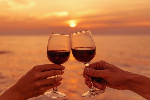 Loving couple clinking glasses with red wine on background of sea at sunset, view of hands, romantic date.