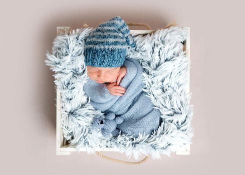 Sweet newborn infant boy is sleeping peacefully while snuggled in blue blankets. Newborn baby sleeping in small box with rabbit toy near him, top view