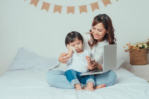 cute little girl and his mother are sitting on the bed and talking by cell phone