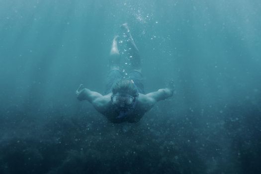 Active male freediver in mask swimming underwater, front view.