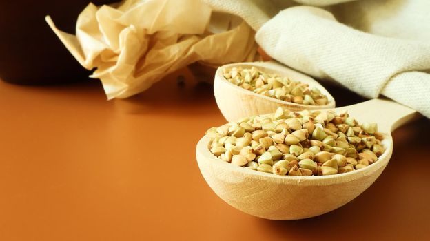Green buckwheat in a wooden spoon on a brown background. Great food. healthy groats. Organic raw non-fried vegetarian food. The concept of a healthy and balanced diet. Dietary foods. Copy space.