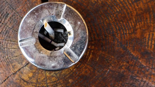 Metal ashtray on a brown wooden table top view. Smoking in public places. Flat lay