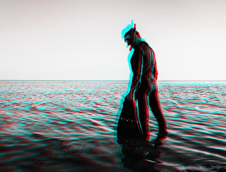 Young man wearing in a diving suit with a mask and flippers standing in the sea over water surface. Image with anaglyph effect.