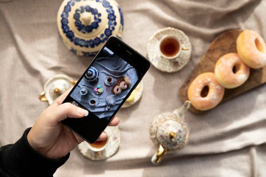 Top view picture of lady,blogger sitting in cafe and making photo with mobile of food, afternoon tea with doughnuts and macarons on the table high angle, food and social media concept close up