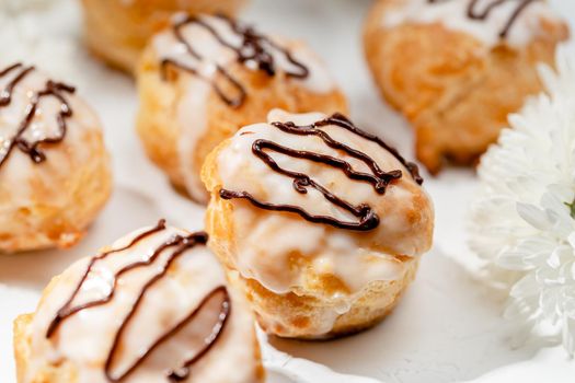 Closeup view of delicious fresh profiteroles filled with custard on white table. Homemade tasty eclairs. Concept of desserts, restaurant food.