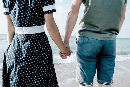 Unrecognizable loving young couple holding hands together in front of sea, rear view.