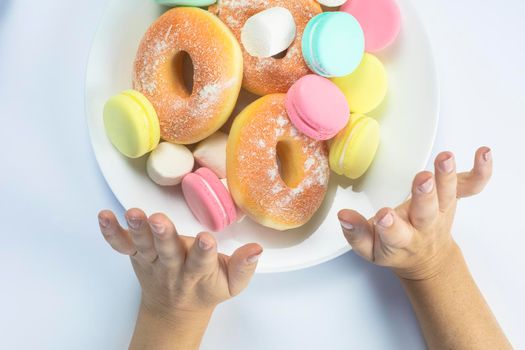 Woman hands making a hand sign of no and refuse for a white plate with fastfood and sugar, top view, healtcare and weightloss concept. donuts, macarons diet sweets