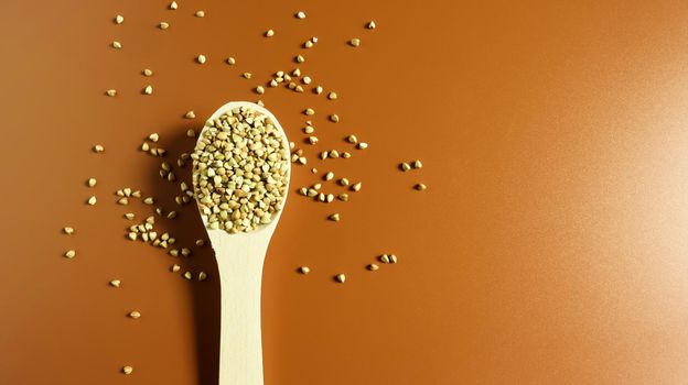 Green buckwheat in a wooden spoon on a brown background. Great food. healthy groats. Organic raw non-fried vegetarian food. The concept of a healthy and balanced diet. Dietary foods. Copy space.