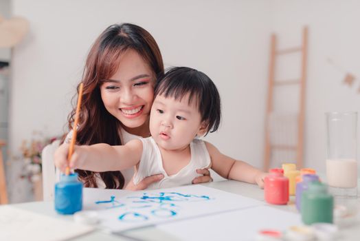 Mother and daughter painting together at home with paintbrushes and watercolors