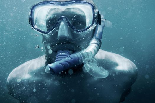 Portrait of young man wearing in mask with snorkel swimming underwater.