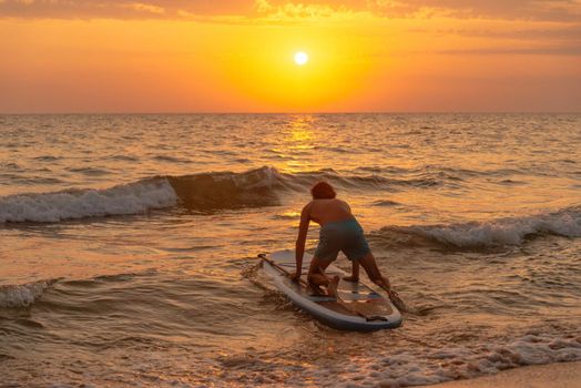 Sporty young man on SUP paddle board going to the sea at sunset.