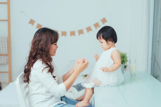 Beautiful young mother smiling while her baby daughter opening birthday gift box.