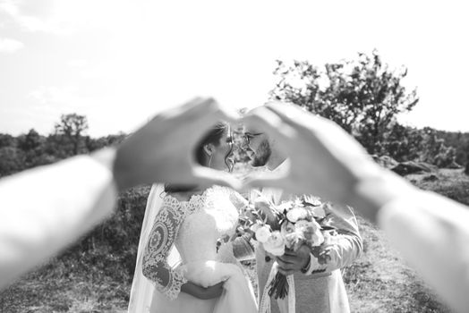 Hands folded in the shape of a heart in which you can see the bearded groom wearing glasses in a gray jacket and bride.