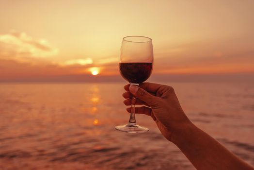 Female hand with glass with red wine on background of sea at sunset.