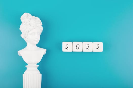 Creative trendy 2022 concept. Numbers written on white cubes next to white antique gypsum woman figure on mint blue background. New year resolution or plans concept