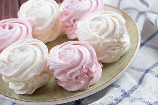 Pink and white meringue cookies on green plate close up