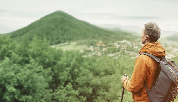 Explorer backpacker young man with trekking poles looking at the mountain outdoor.