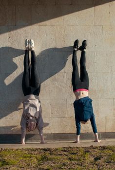 Two young women acrobat doing handstand on the wall with cityscape on background, close up