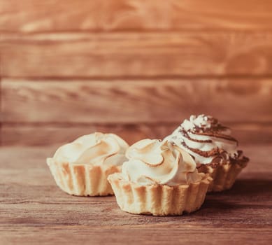 Three holiday sweet cupcakes with whipped cream on a wooden background.