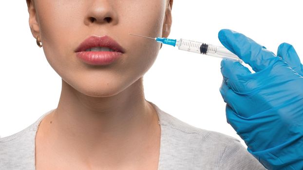 Beauty injections. Close-up view - gloved hands with a syringe inject Botox into the nasolabial wrinkles. Isolated on white.