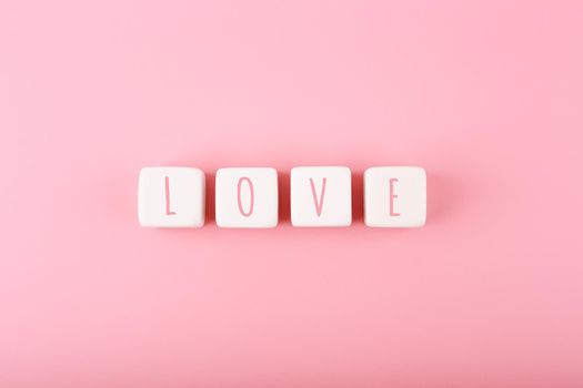 Word love written on white toy cubes against pink background with copy space. Minimal trendy concept of Valentine's day, love emotions, anniversary or dating