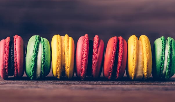 Sweet dessert macaroons of different colors in a row on wooden background, close-up.