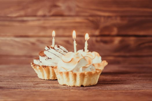 Three holiday birthday cupcakes with burning candles on a wooden background.