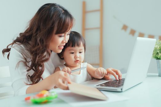 Stay at home mom working remotely on laptop while taking care of her baby.