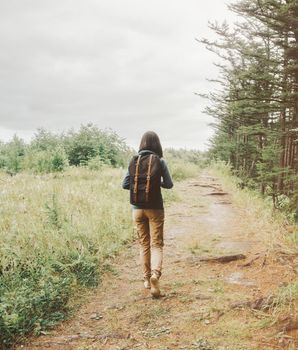 Backpacker girl walking on footpath in summer forest, rear view.