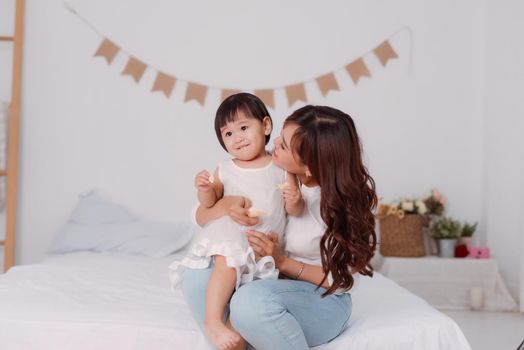 happy young woman playing with adorable toddler 1 year old girl, relaxing on the bed