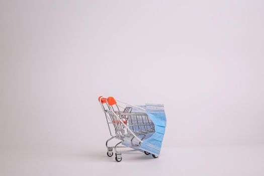 Safe and online shopping on quarantine concept. Shopping cart with protective medical mask against coronavirus. White background, copy space.