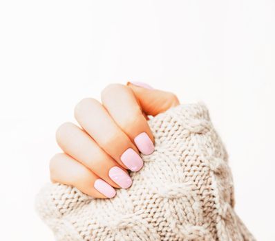 Woman’s hand with manicure of pink pastel color and art design wearing in wool sweater, nail polish.