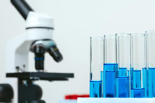 Microscope and colored test tubes on table in laboratory, close up