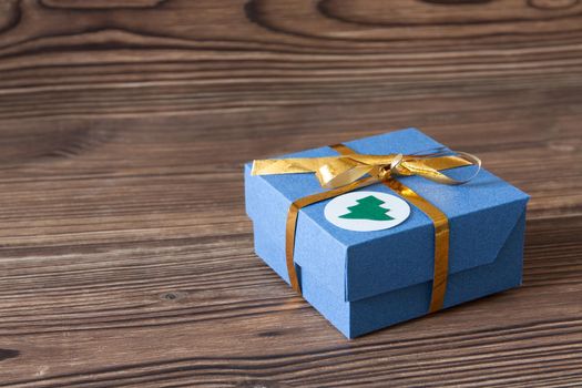 Blue gift box with golden ribbon on a brown wooden background for Christmas and New Year