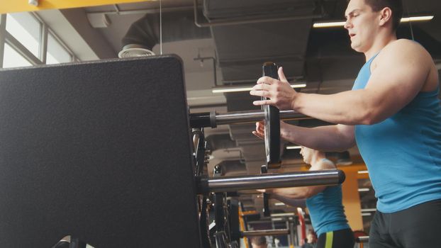 Muscular sporty man add weight for squats machine in the gym, close up view