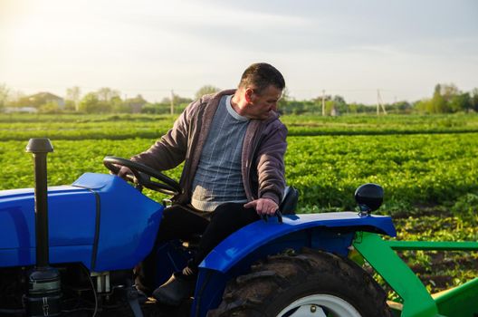 A farmer drives a tractor while harvesting potatoes. First potato harvest in early spring. Agro industry and agribusiness. Harvesting mechanization in developing countries. Farming and farmland.