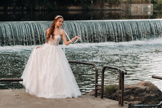 An elegant bride in a white dress and gloves stands by the river in the Park, enjoying nature.A model in a wedding dress and gloves in a nature Park.Belarus.