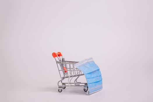 Safe and online shopping on quarantine concept. Shopping cart with protective medical mask against coronavirus. White background, copy space.