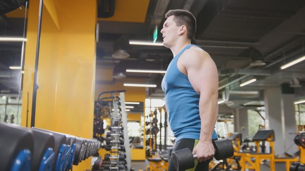 Bodybuilding in the gym - young sporty man performs training for arm, telephoto